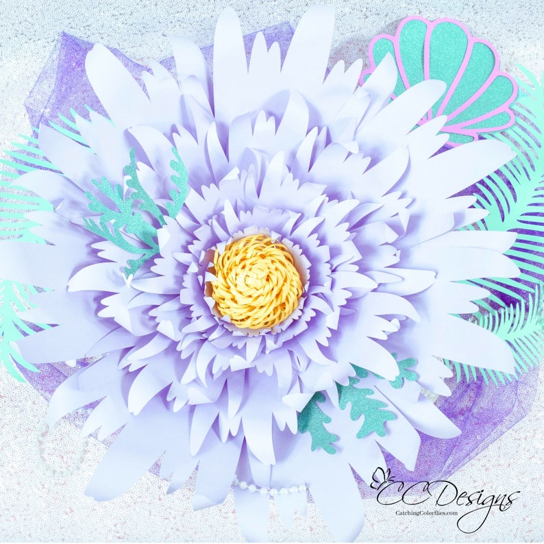 May include: A large, lavender paper flower with a yellow center. The flower is surrounded by green paper leaves and a seashell.