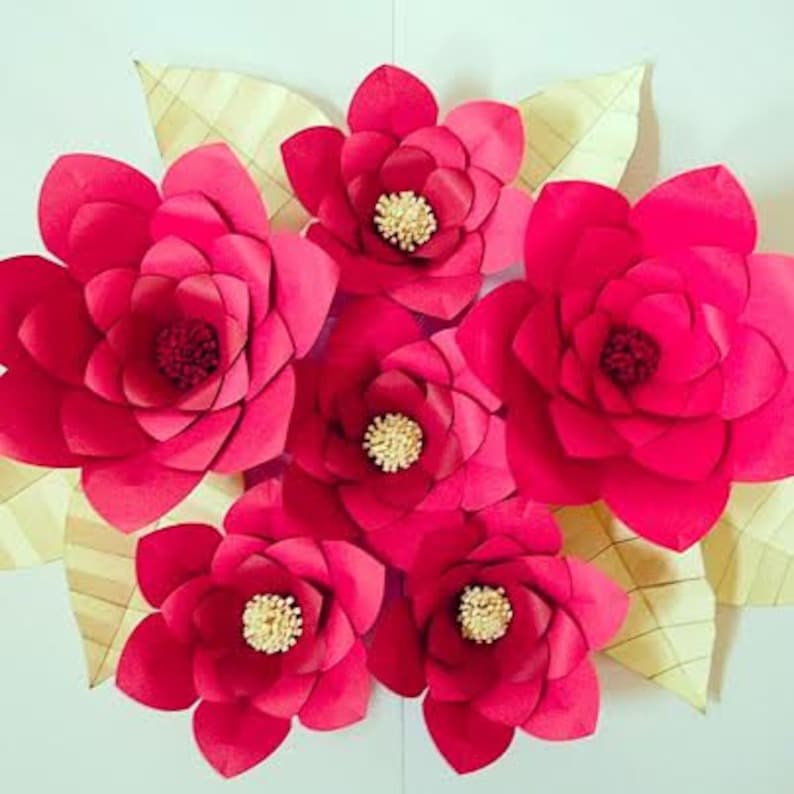 May include: A cluster of six large, paper flowers in shades of pink and red. The flowers are arranged in a circle with the largest flower in the center. The flowers are made of paper and have a layered, ruffled appearance.