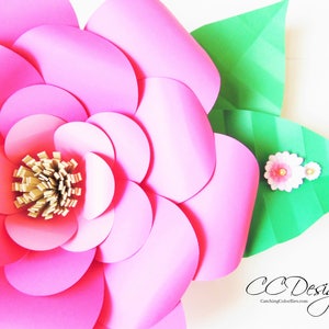 May include: A large pink paper flower with a gold center and green leaves. The flower is made of multiple layers of paper circles.