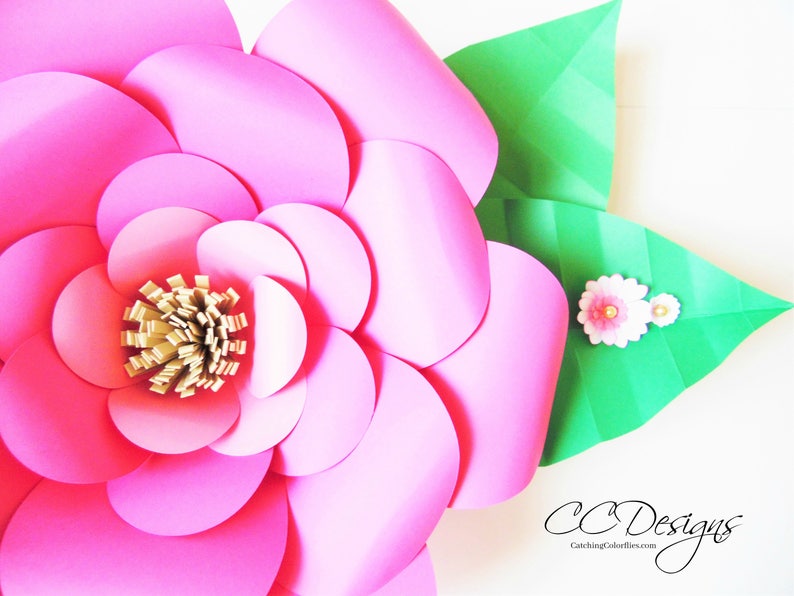 May include: A large pink paper flower with a gold center and green leaves. The flower is made of multiple layers of paper circles.