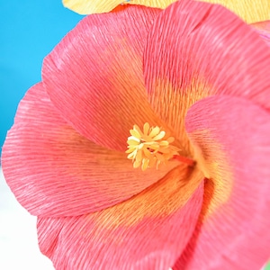 Puede incluir: Primer plano de una flor de papel rosa y amarilla con un centro amarillo. La flor est&aacute; hecha de papel de seda arrugado y tiene una textura delicada y en capas.