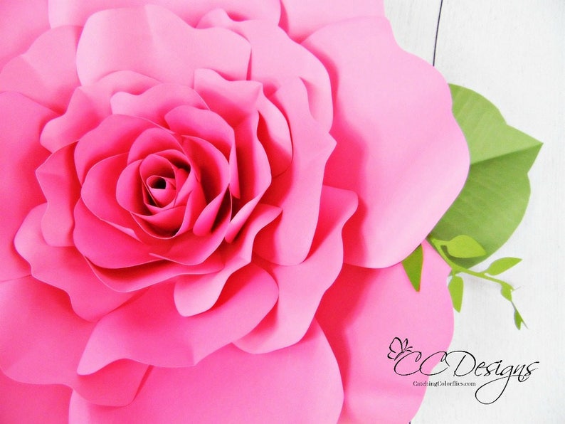 May include: A large, pink paper rose with a green stem and leaves. The rose is made of multiple layers of paper, creating a 3D effect.