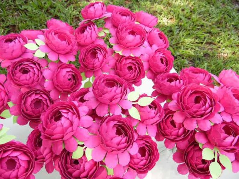 May include: A bouquet of pink paper flowers, each with multiple layers of petals, arranged in a semi-circle.
