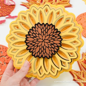 K&ouml;nnte beinhalten: Eine mehrschichtige Papier-Sonnenblume mit braunem Zentrum und goldenen Akzenten. Die Sonnenblume besteht aus mehreren Papierschichten, die einen 3D-Effekt erzeugen.