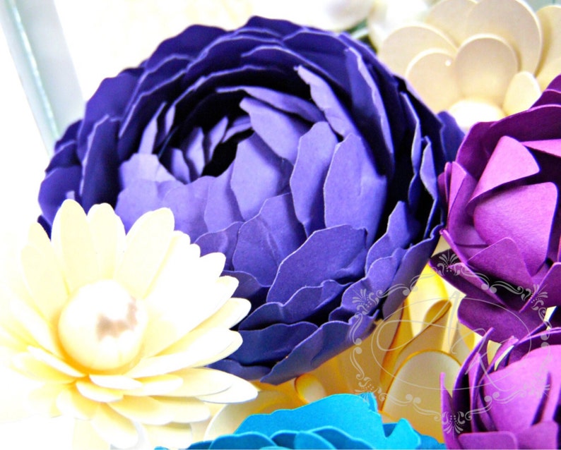 May include: A bouquet of paper flowers in shades of purple, yellow, and blue. The flowers are arranged in a vase and are a beautiful example of paper crafting.
