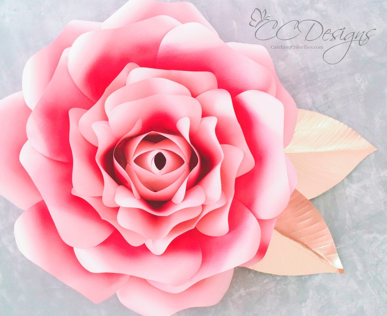 May include: A large, pink paper rose with a layered, ruffled center. The rose is accented with two gold paper leaves.