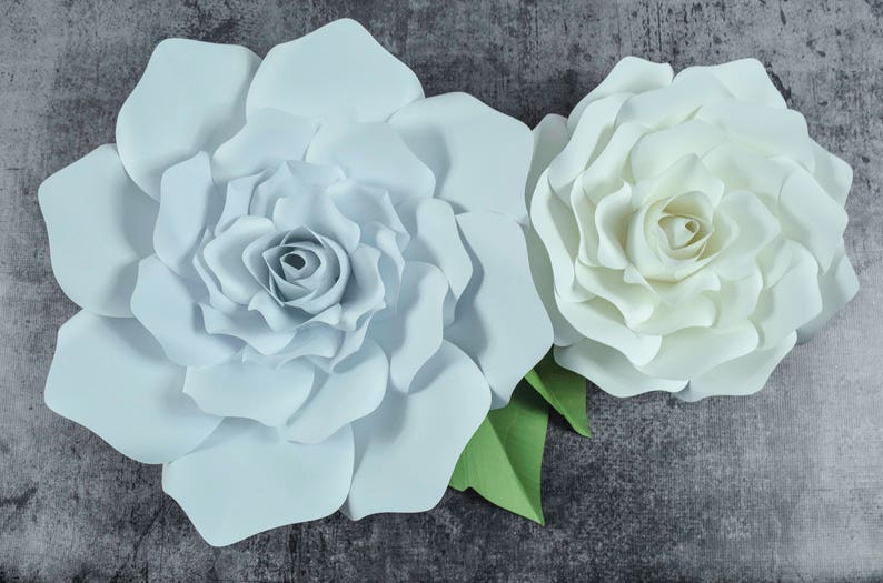 May include: Two large paper flowers, one light blue and one white, with green leaves. The flowers are made of paper and have a layered, ruffled appearance.