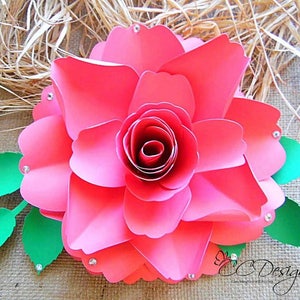 May include: A large, pink paper rose with a green leaf stem. The rose is made of multiple layers of paper and has a center that is curled inward. The rose is decorated with small, clear rhinestones.