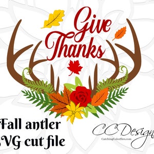 May include: A digital cut file design featuring a pair of brown antlers with fall foliage, a red rose, yellow flowers, and green ferns. The text "Give Thanks" is written in red cursive lettering.