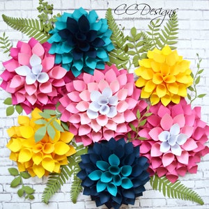 May include: A wall decor featuring seven paper flowers in various colors, including pink, yellow, teal, and navy blue. The flowers are arranged in a circular pattern on a white brick wall background. The flowers are made of paper and have a 3D effect.
