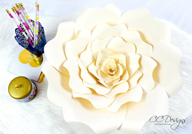 May include: A large, white paper flower with multiple layers of petals. The flower is in focus and the background is blurred.