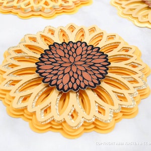 K&ouml;nnte beinhalten: Mehrschichtige Papier-Sonnenblume mit braunem und schwarzem Zentrum. Die Sonnenblume besteht aus gelbem Papier mit goldenen Glitzerakzenten.