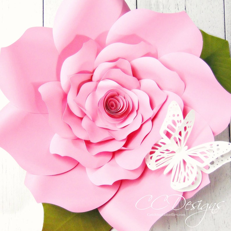 May include: A large pink paper flower with a white butterfly on the side. The flower is made of multiple layers of paper and has a spiral center. The butterfly is delicate and intricate.