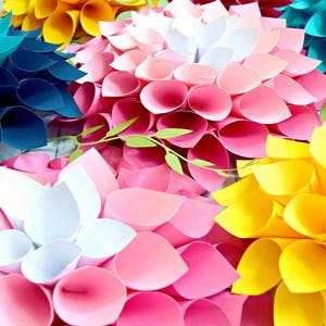 May include: A collection of paper flowers in various colors, including teal, yellow, pink, and white. The flowers are made of folded paper and have a layered, three-dimensional appearance.