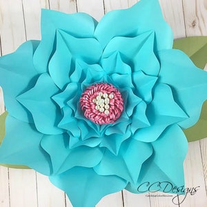 May include: A large, teal paper flower with a pink center and white pearl accents. The flower is made of multiple layers of paper and has a delicate, layered look.