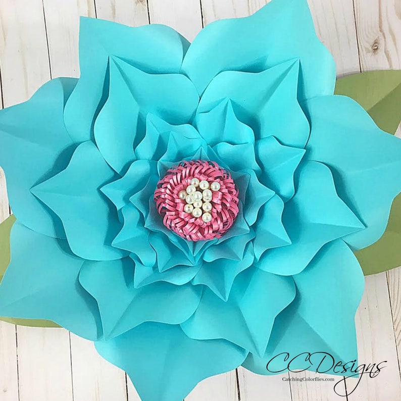 May include: A large, teal paper flower with a pink center and white pearl accents. The flower is made of multiple layers of paper and has a delicate, layered look.