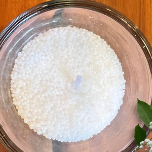May include: A white candle in a clear glass jar. The candle is made of small white beads and has a blue wick.