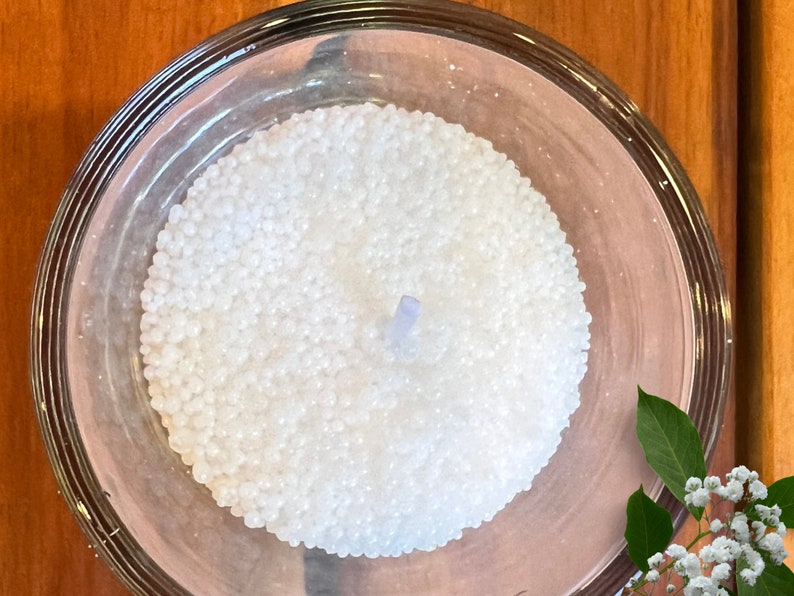 May include: A white candle in a clear glass jar. The candle is made of small white beads and has a blue wick.
