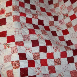 Pode incluir: Um edredom feito à mão com um design de patchwork. O edredom apresenta um padrão de quadrados vermelhos e brancos alternados. Alguns quadrados têm tecido floral ou estampado. O edredom tem uma borda vermelha.