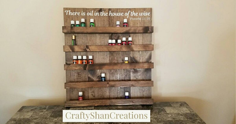 May include: Wooden shelf unit with five shelves for storing essential oil bottles. The shelf has a rustic brown finish and the text "There is oil in the house of the wise Proverbs 21:20" is printed on the top shelf.