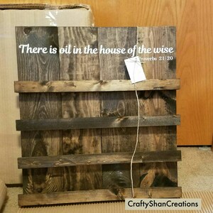May include: A rustic wooden sign with the text "There is oil in the house of the wise" and the scripture reference "Proverbs 21:20". The sign has a dark brown stain and is made of reclaimed wood.