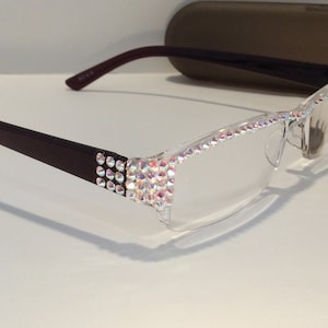 May include: A pair of clear reading glasses with a brown frame. The frame is decorated with iridescent rhinestones.