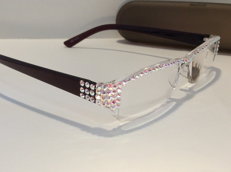 May include: A pair of clear reading glasses with a brown frame. The frame is decorated with iridescent rhinestones.