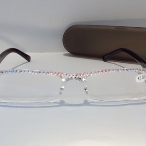 May include: Clear reading glasses with a black frame and rhinestones around the edges. The glasses have a +2.50 lens strength.