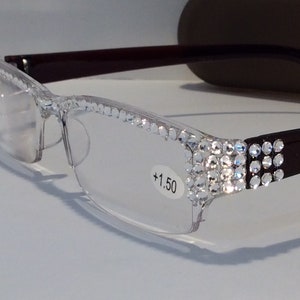 May include: Clear reading glasses with a burgundy frame and rhinestones on the temples. The glasses have a +1.50 lens strength.