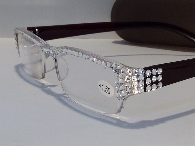 May include: Clear reading glasses with a burgundy frame and rhinestones on the temples. The glasses have a +1.50 lens strength.