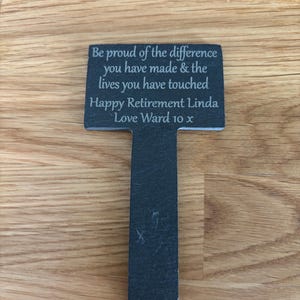 May include: A T-shaped slate garden marker with engraved text that reads: Be proud of the difference you have made & the lives you have touched. Happy Retirement Linda. Love Ward 10 x. The dark gray stone has a natural texture and a pointed bottom stake.