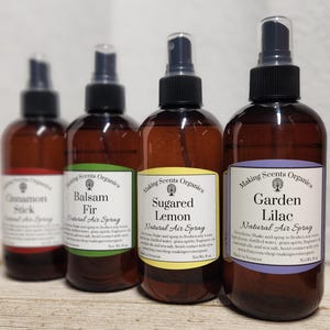 May include: Four brown glass spray bottles with black caps and white labels. The labels read "Cinnamon Stick", "Balsam Fir", "Sugared Lemon", and "Garden Lilac" with "Natural Air Spray" below. Each bottle is 8 oz.