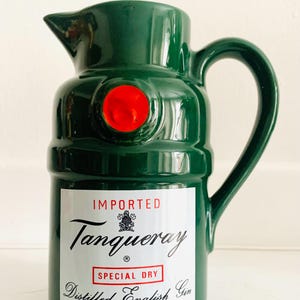 May include: A green ceramic pitcher with a handle and spout, featuring a red circular accent. The pitcher has a label with the text "Tanqueray Special Dry Distilled English Gin" and is marked "Imported".