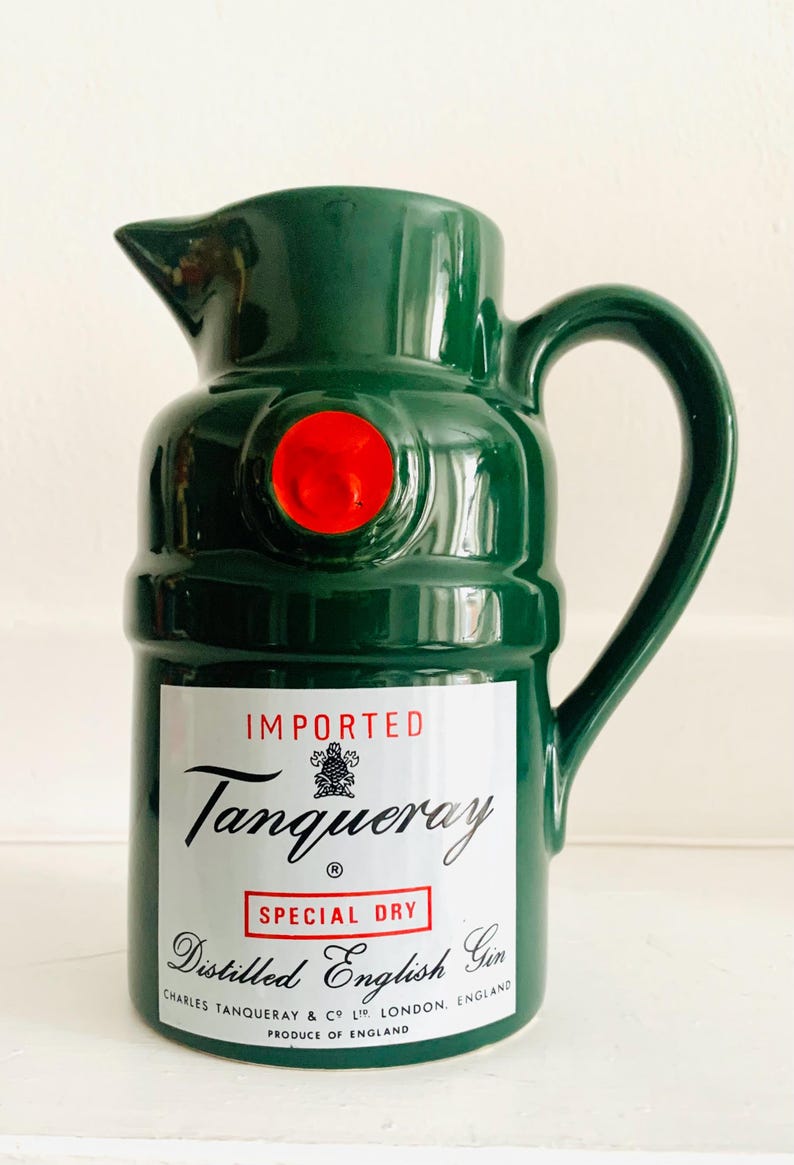 May include: A green ceramic pitcher with a handle and spout, featuring a red circular accent. The pitcher has a label with the text "Tanqueray Special Dry Distilled English Gin" and is marked "Imported".