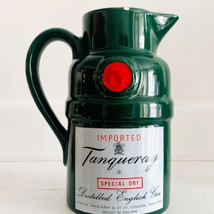 May include: A green ceramic pitcher with a handle and spout, featuring a red circular accent. The pitcher has a label that reads "IMPORTED Tanqueray SPECIAL DRY Distilled English Gin."