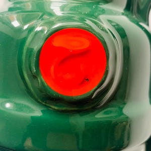 May include: Close-up of a green ceramic bottle with a bright red circular detail. The word "IMPORTED" is printed in red on the bottle. The bottle has a glossy finish.