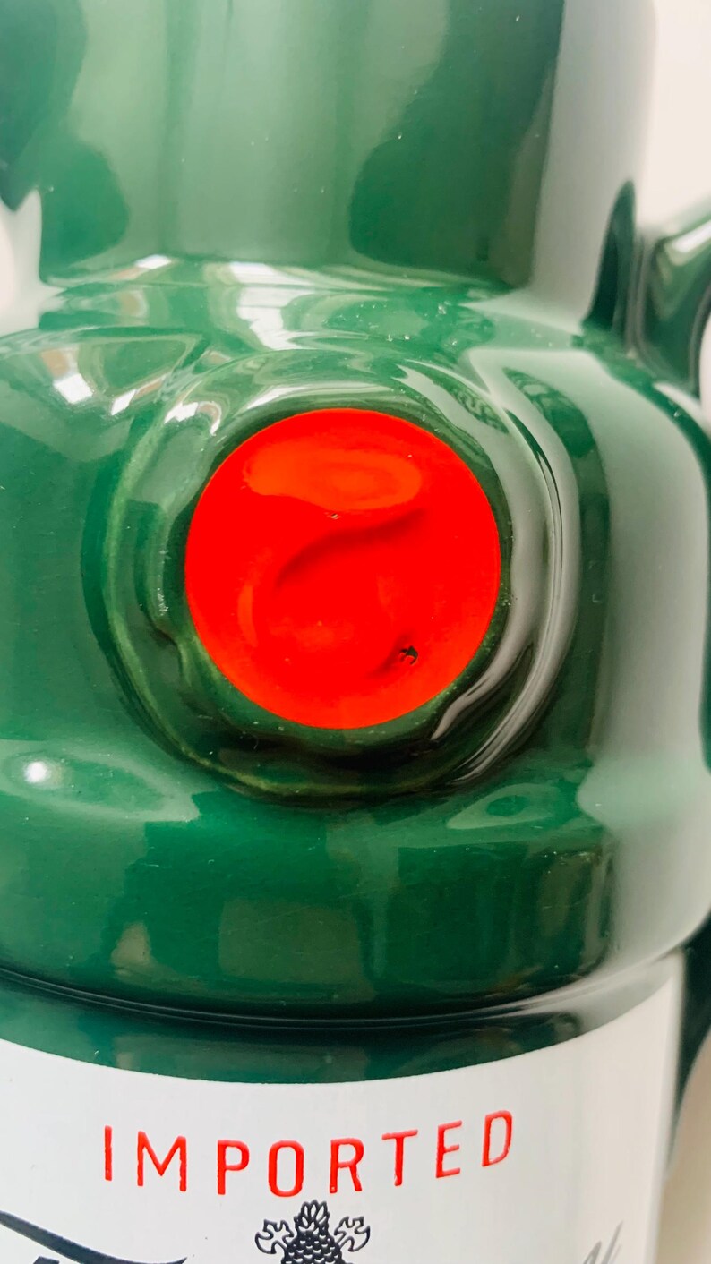 May include: Close-up of a green ceramic bottle with a bright red circular detail. The word "IMPORTED" is printed in red on the bottle. The bottle has a glossy finish.