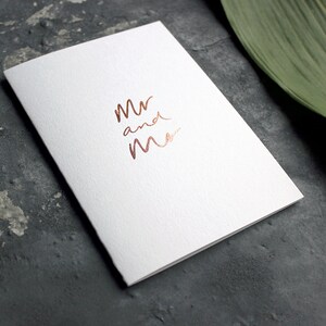 May include: A white card with the words "Mr and Mrs" written in rose gold foil.