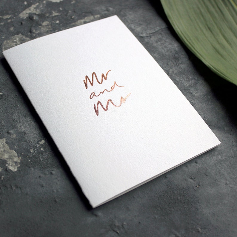 May include: A white card with the words "Mr and Mrs" written in rose gold foil.