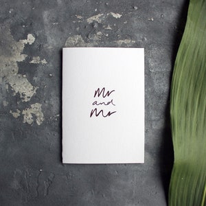 May include: White card with the text "Mr and Mr" written in dark purple ink.