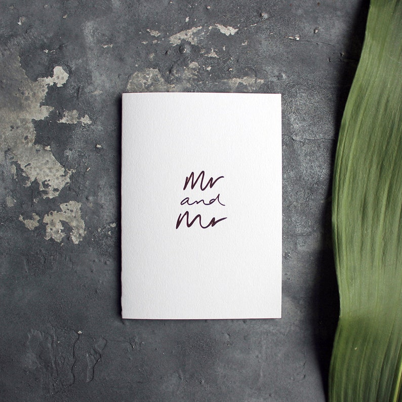 May include: White card with the text "Mr and Mr" written in dark purple ink.
