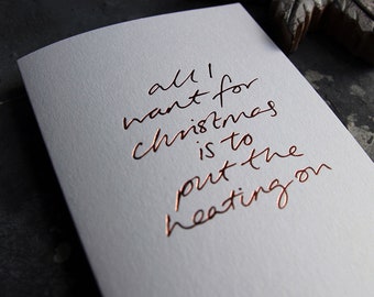 Könnte beinhalten: Eine weiße Karte mit dem Text "all I want for christmas is to put the heating on" in kupferfarbener Schrift.