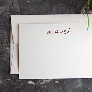 May include: A white card with a red cursive inscription that says "merci".