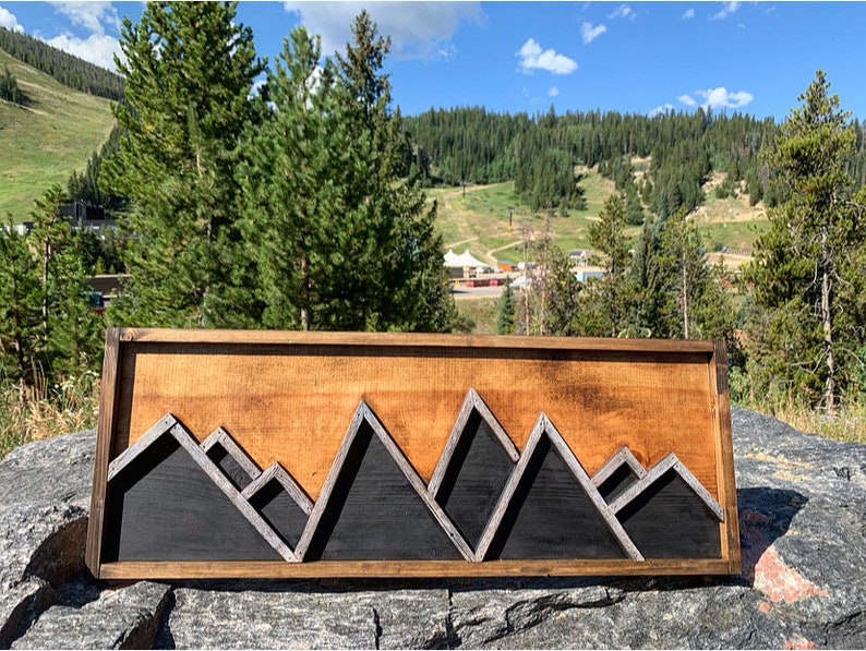 May include: A wooden wall art piece featuring a mountain range silhouette. The mountains are made of black wood with silver accents and are set against a light wood background.