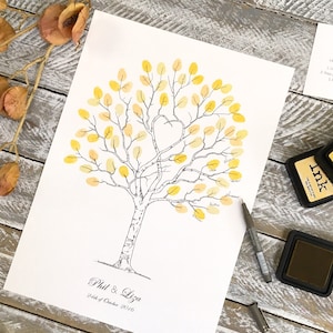 Può includere: Un foglio di carta bianco con un disegno in bianco e nero di un albero con foglie gialle. Le foglie sono riempite con impronte digitali gialle. Il testo "Phil & Liza 24th of October 2016" è in fondo alla pagina.