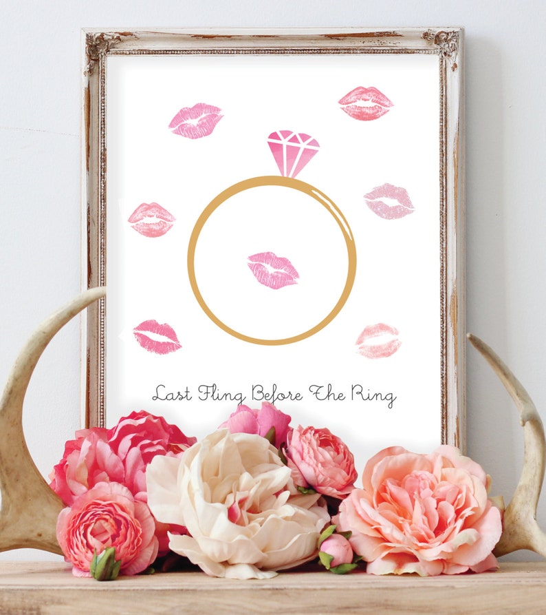 May include: A white framed print with a gold ring and a diamond in the center. Pink lips are printed around the ring. The text "Last Fling Before The Ring" is printed below the ring.