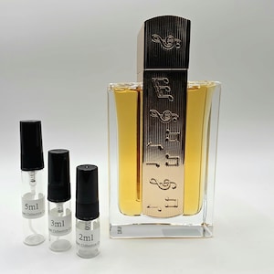 May include: A perfume bottle with a gold-colored cap and a clear, rectangular body. The bottle has a gold label with musical notes. Three small sample bottles are in front of the perfume bottle, with black caps and labels indicating their sizes: 5ml, 3ml, and 2ml.