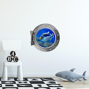 May include: A silver porthole with a blue background and a black and white fish swimming inside. The porthole is a wall decal.