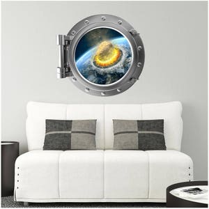 May include: A silver porthole wall decal with a view of a meteor hitting Earth. The decal is on a white wall above a white couch with two gray pillows.