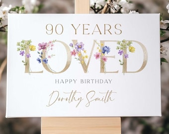 May include: A white canvas sign with gold lettering that reads "90 Years Loved" with floral accents. The sign also says "Happy Birthday Dorothy Smith".